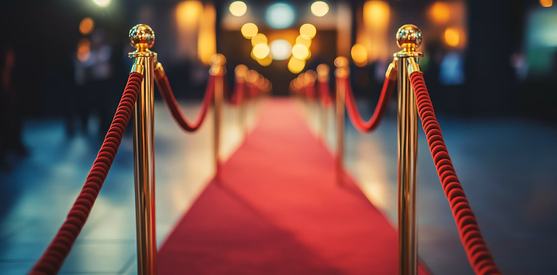 A red carpet running between stanchions and velvet rope toward the lights of an entrance